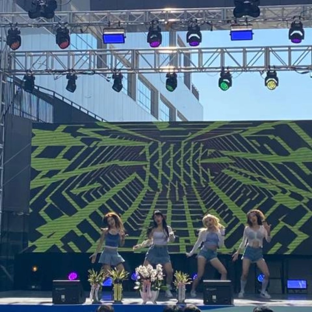 야외 트러스 무대 위 LED 화면 앞에서 댄서 네 명이 같은 동작으로 춤추고 있다