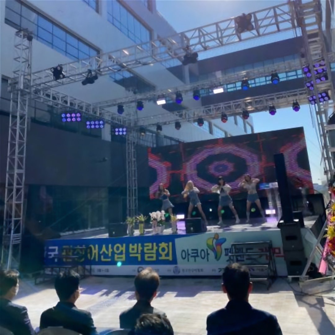 정장을 입은 내빈들이 의자에 앉아 무대를 보고 있고 무대에는 행사 현수막이 걸려 있다