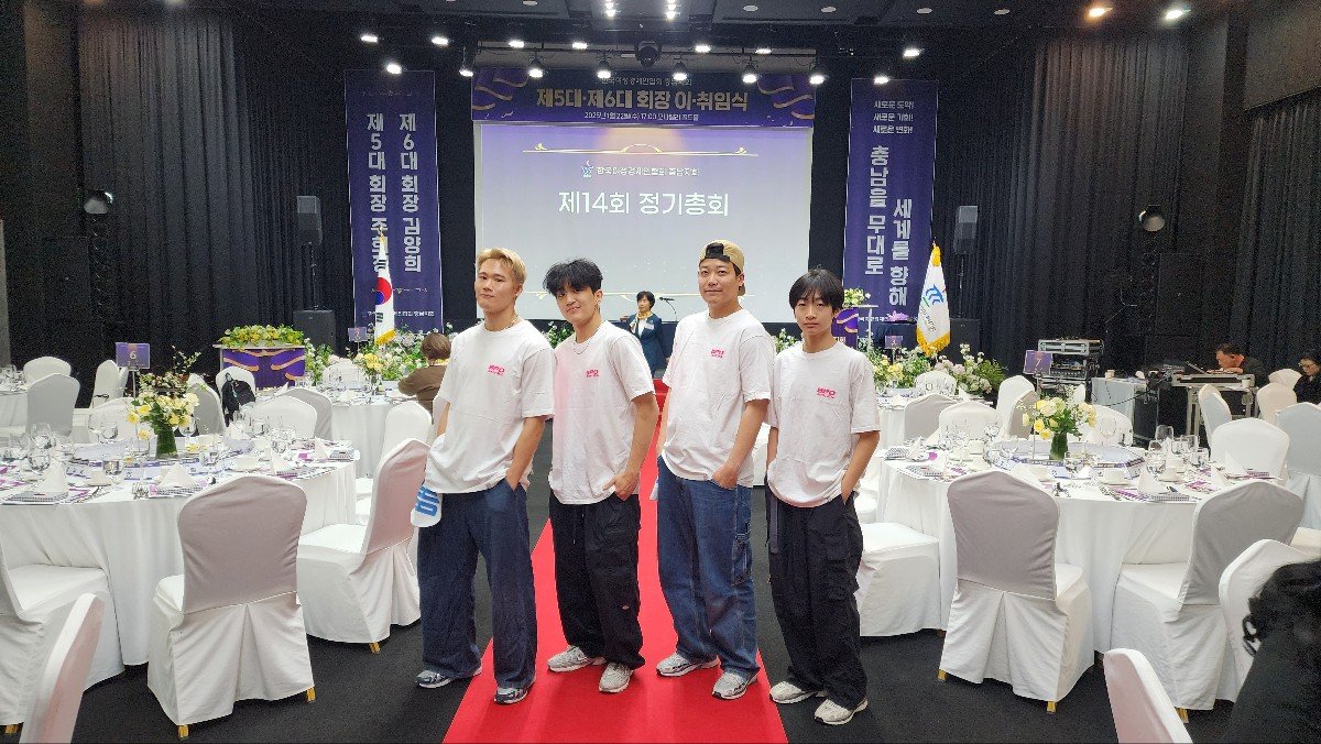흰 셔츠와 통 넓은 바지를 입은 남성 댄서 세 명이 라운드 테이블이 놓인 홀의 레드카펫 위에 서 있다
