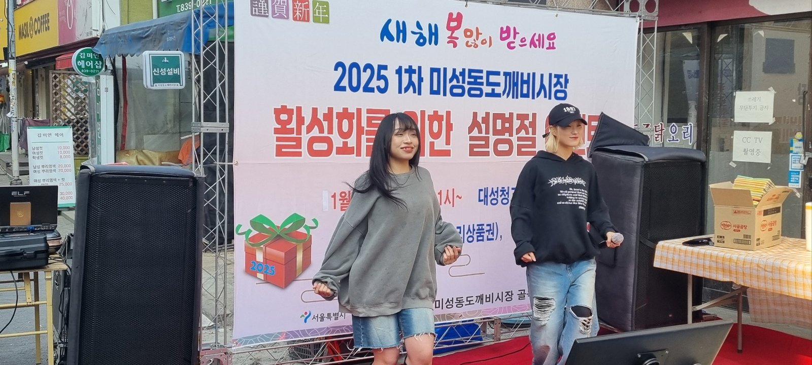 설명절 이벤트 현수막 앞 레드카펫 위에서 회색 후드와 검은 옷을 입은 댄서 두 명이 춤을 추고 있다