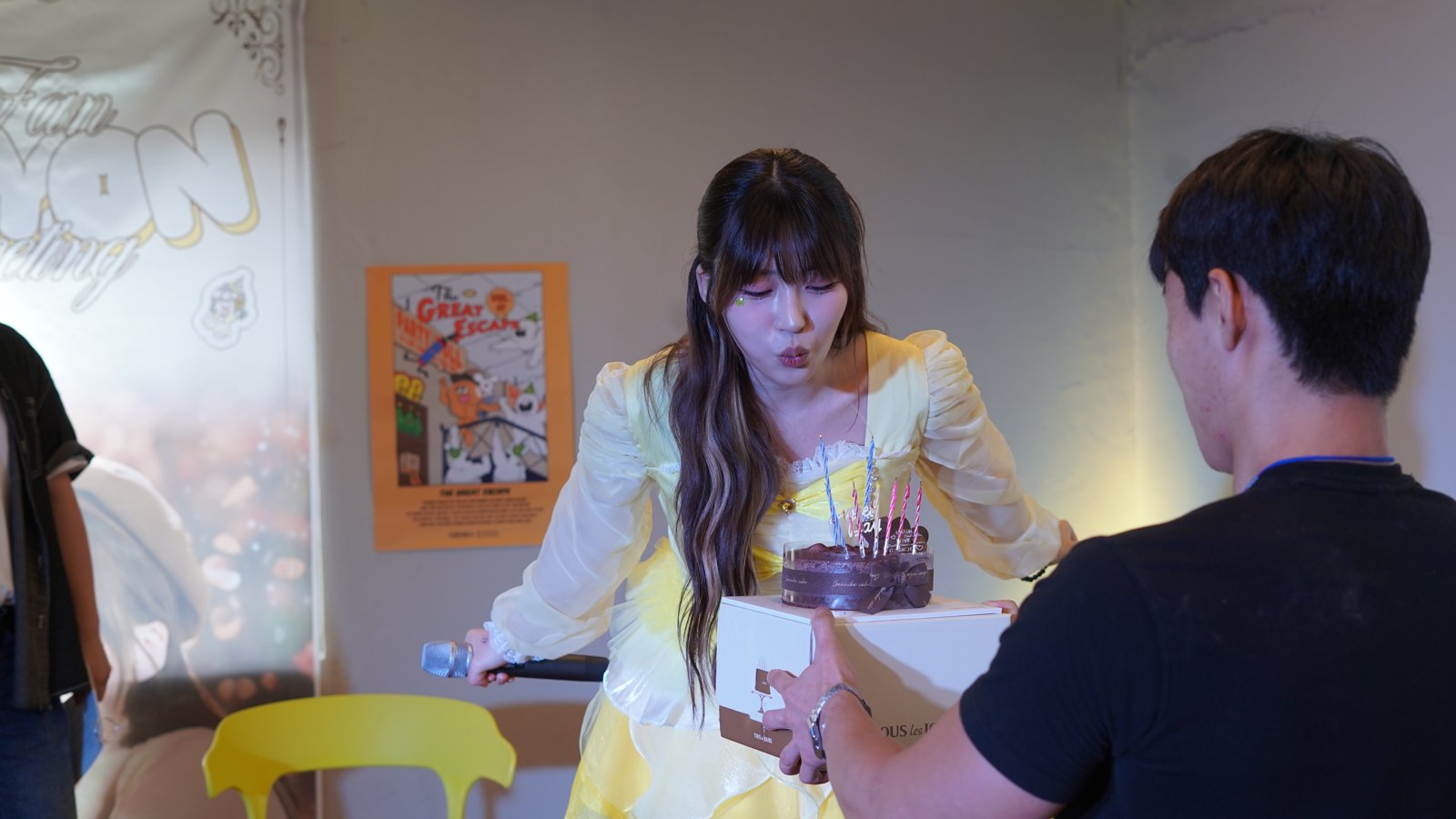 무대 위에서 조이온이 초를 꽂은 초콜릿 케이크 앞에서 촛불을 끄려 하고 스태프가 케이크를 들고 있다