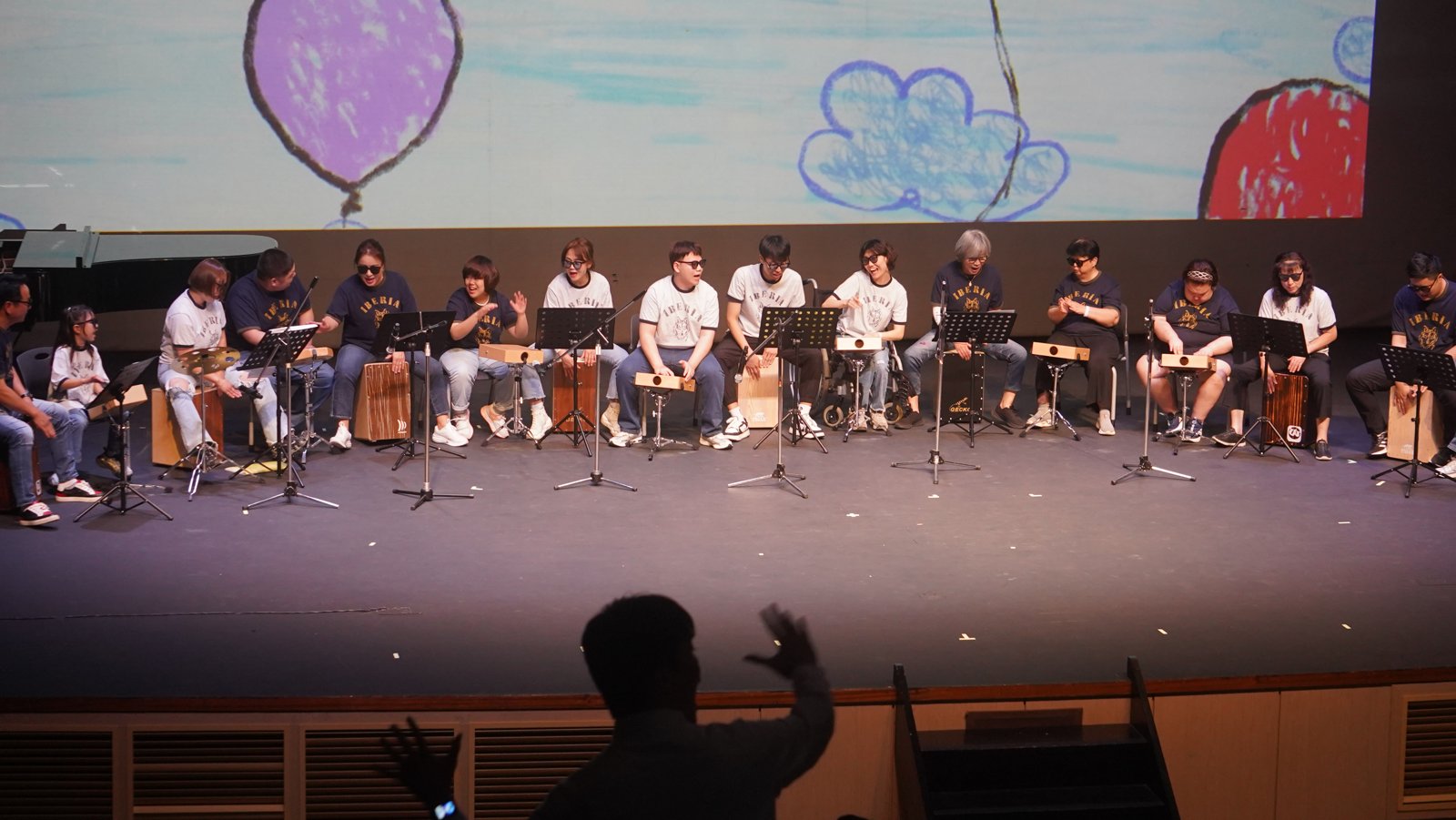 무대 위에 의자를 일렬로 놓고 앉은 연주자들이 카혼과 타악기를 연주하고 있다