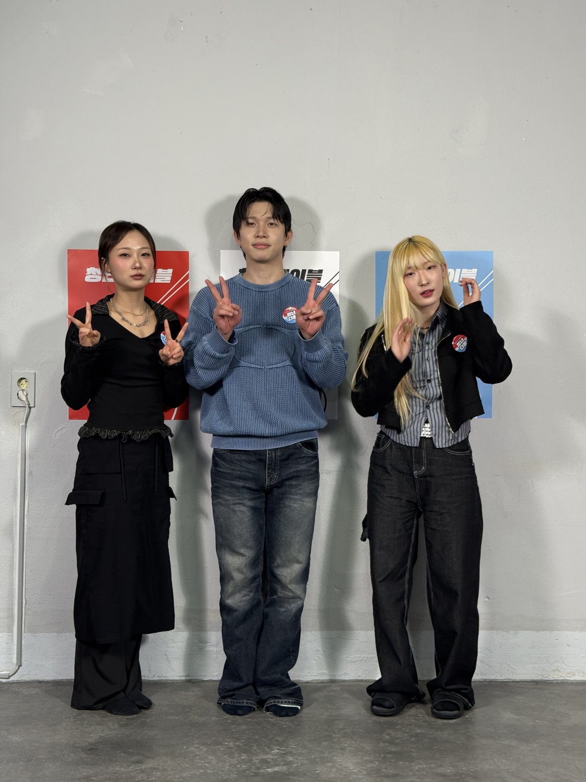 청년다방 포스터 세 장이 붙은 흰 벽 앞에 출연진 세 명이 손가락 포즈를 하고 서 있는 전신 사진