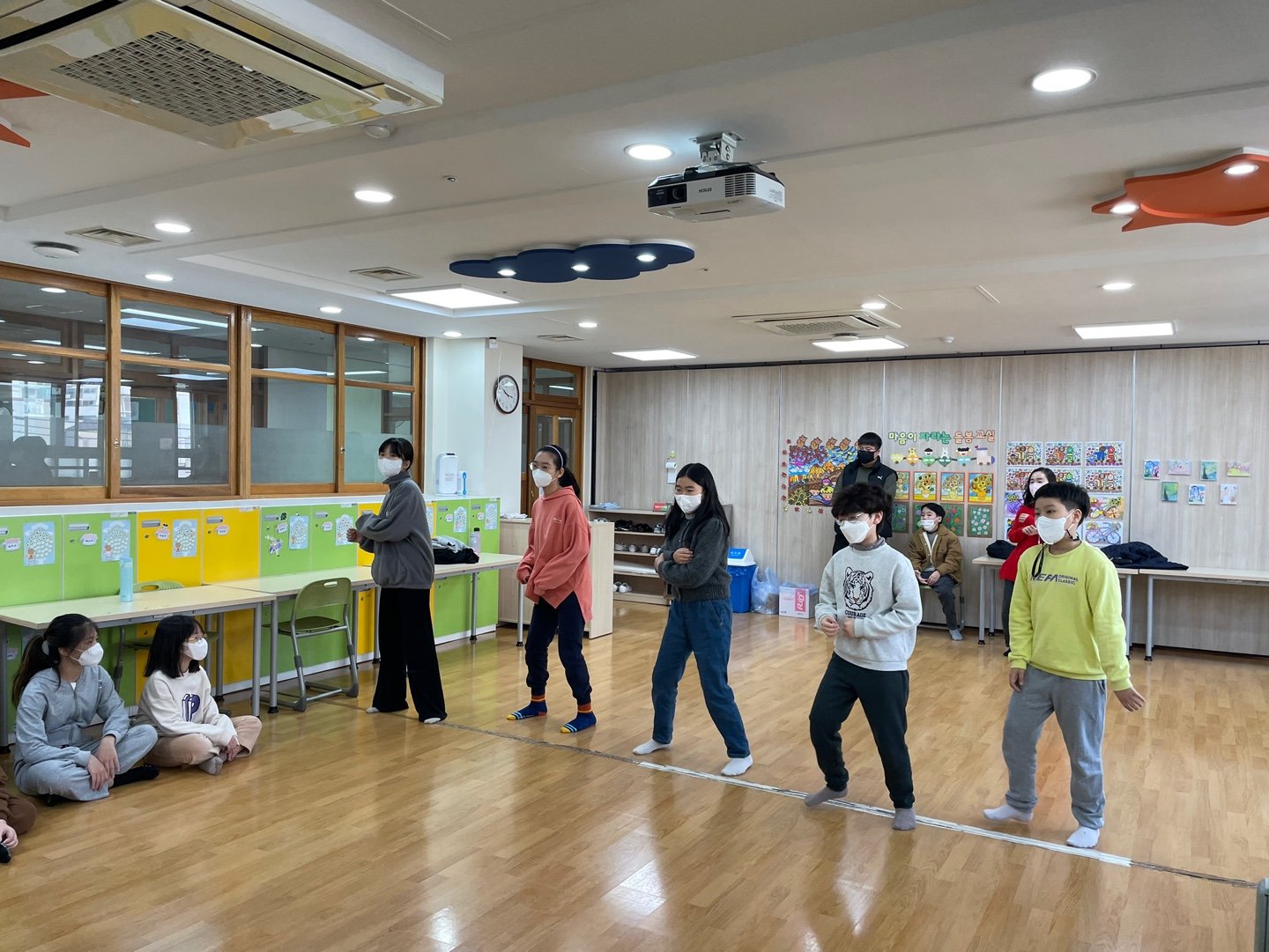 교실에서 마스크를 쓴 초등학생들이 줄지어 서서 강사의 움직임을 따라 하고 있다