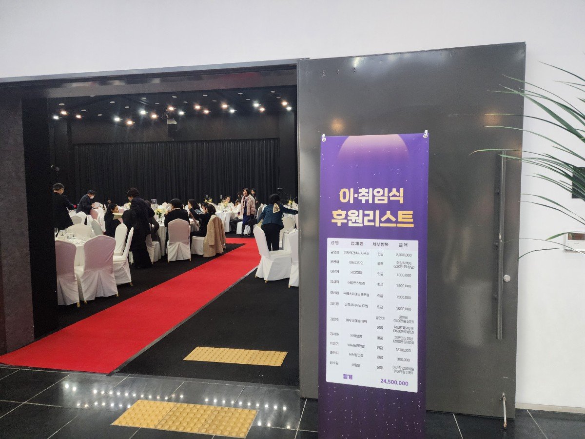 검은 문 옆에 이·취임식 후원리스트라고 적힌 보라색 배너가 서 있고 안쪽으로 레드카펫과 라운드 테이블이 보인다