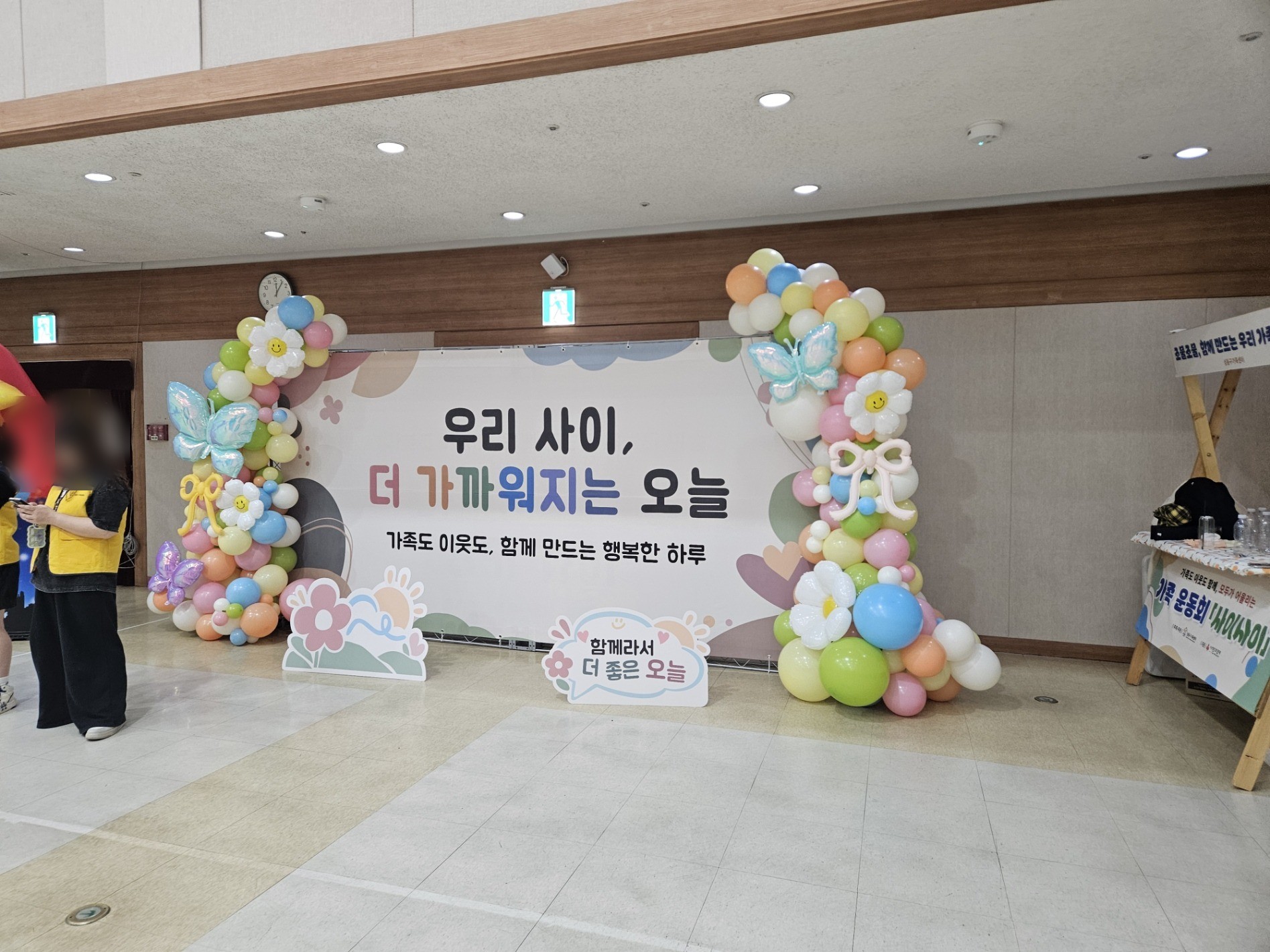 우리 사이 더 가까워지는 오늘 문구의 현수막 양옆으로 풍선 기둥이 선 포토월. 인물 얼굴은 흐리게 처리했다