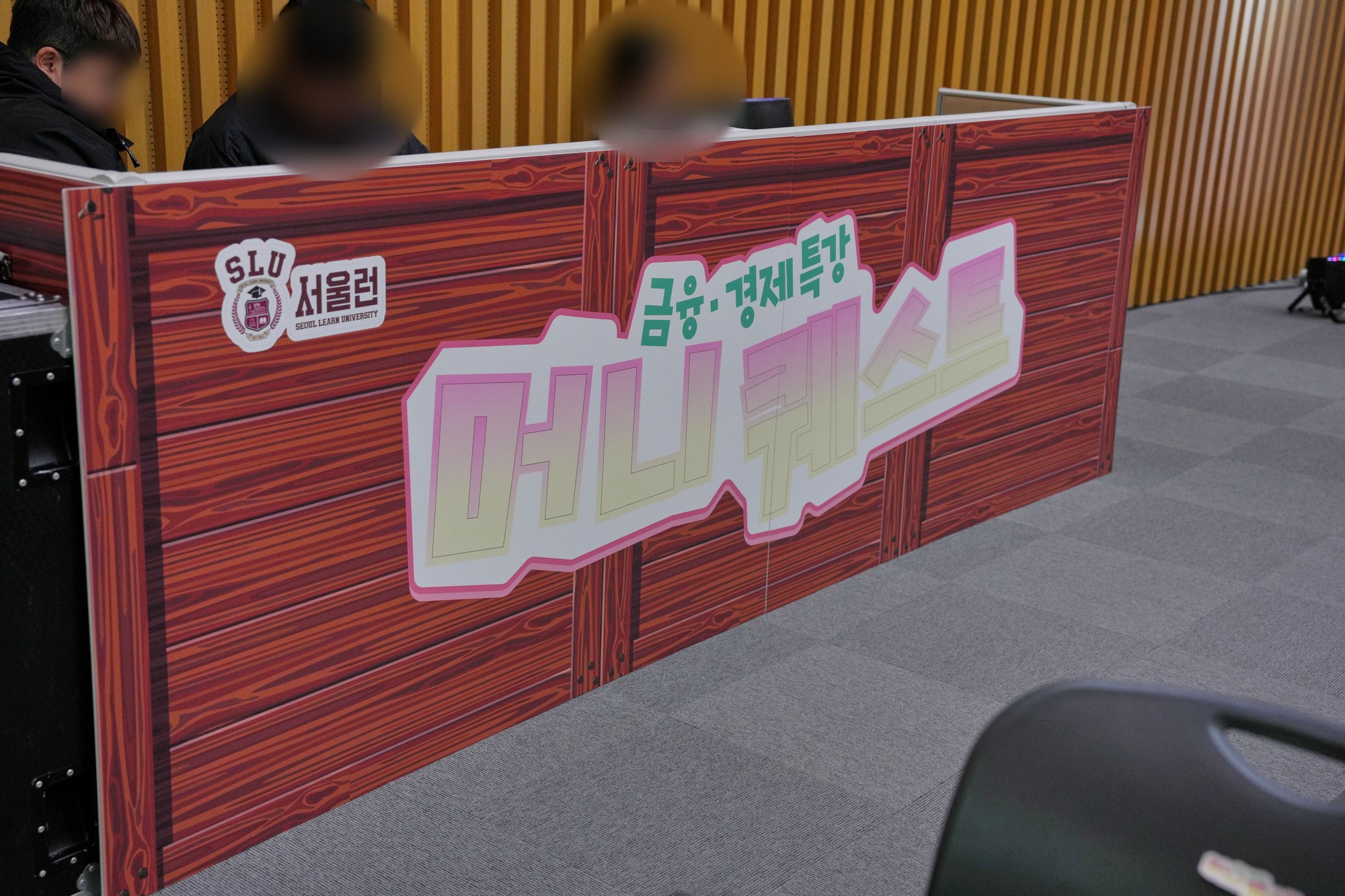 서울런 로고와 금융·경제특강 머니 퀘스트 문구가 인쇄된 나무 무늬 폼보드로 감싼 등록 데스크. 인물 얼굴은 흐리게 처리했다