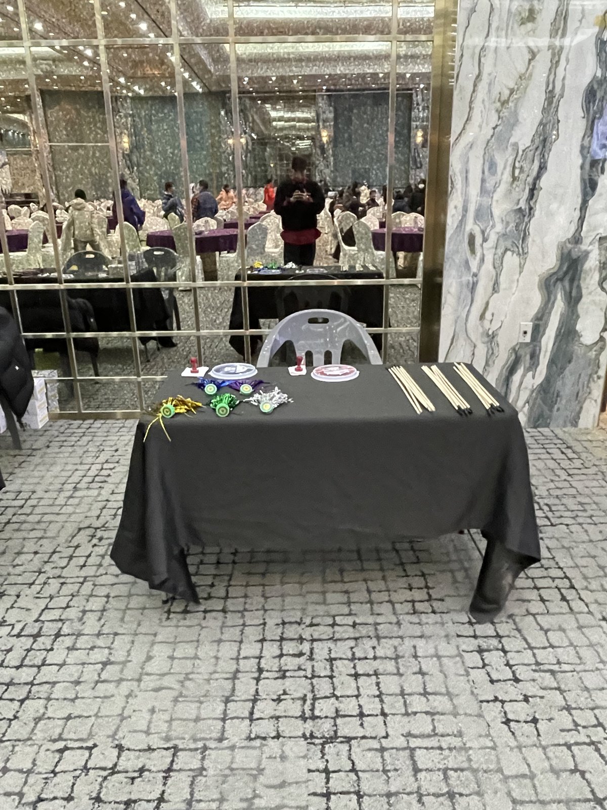 거울 벽 앞 검은 천을 씌운 테이블 위에 제기 여러 개와 달고나 틀, 도장, 나무 막대가 놓여 있고 거울에 연회장 테이블이 비친다