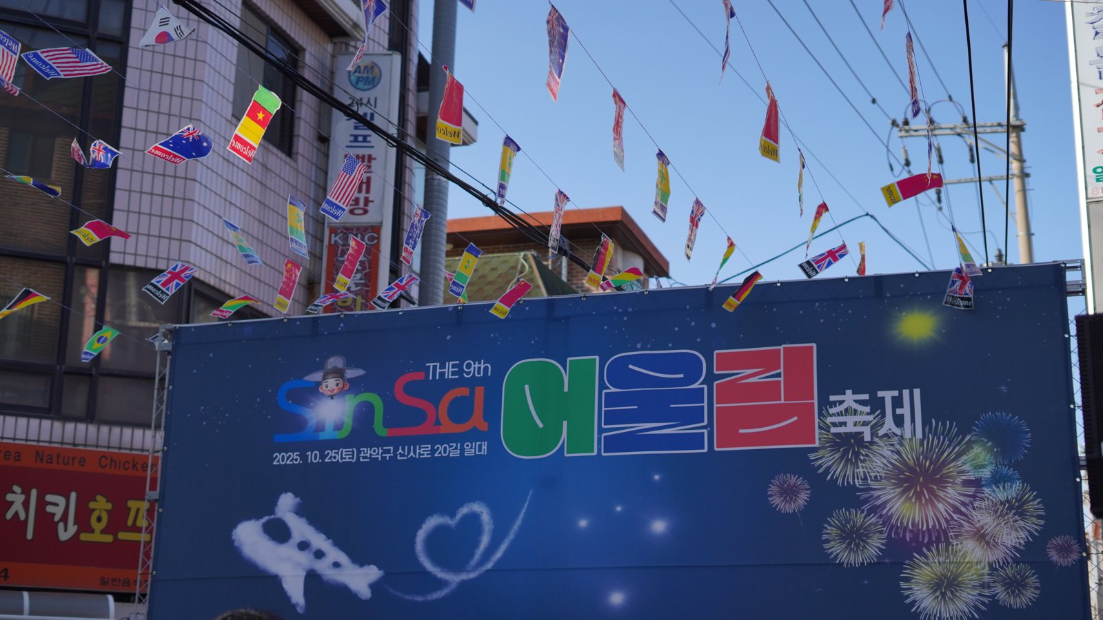 만국기 아래 푸른 바탕에 SinSa 어울림 축제 로고와 불꽃 그래픽을 넣은 무대 백월이 서 있다