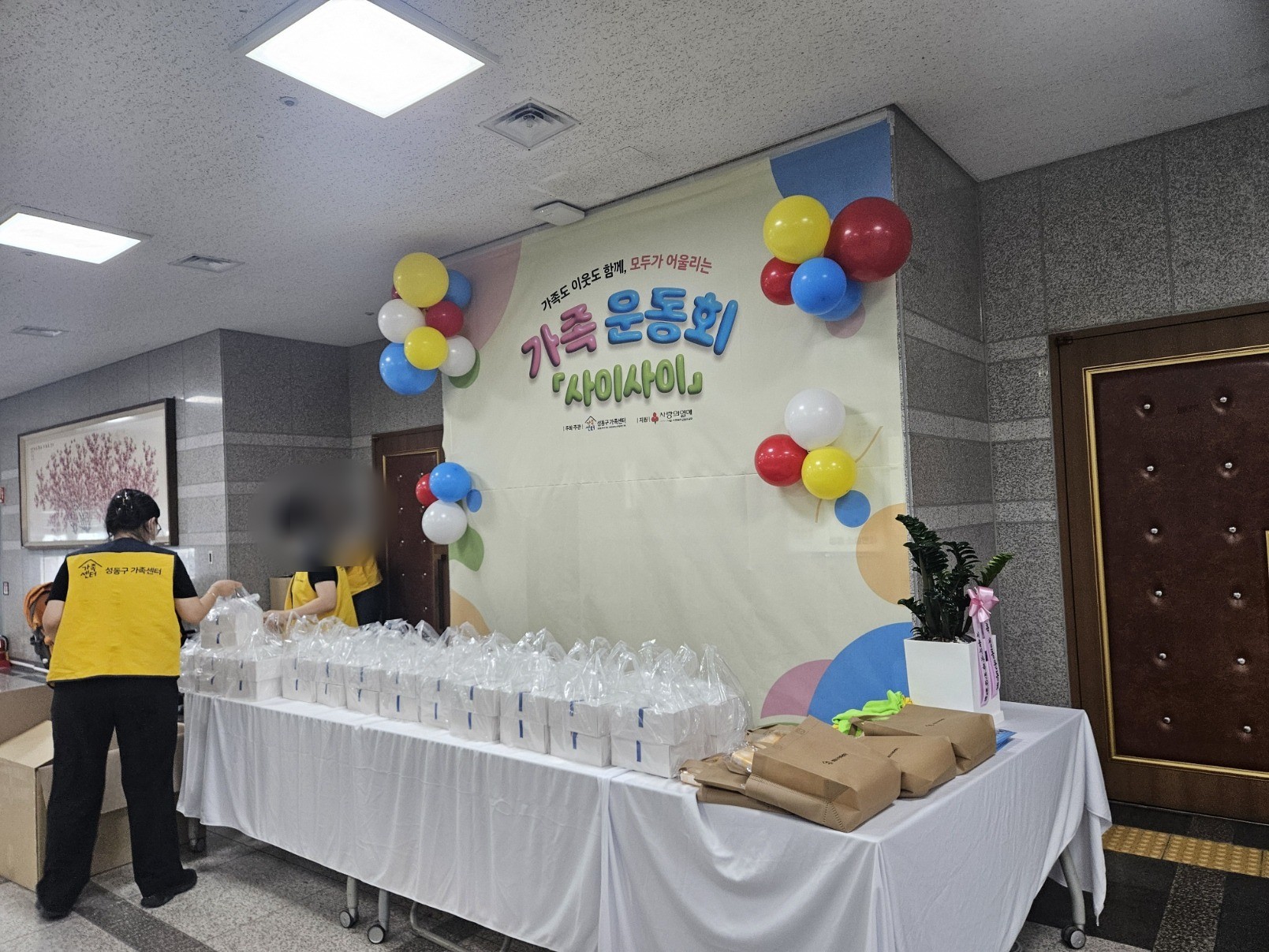 성동구청 로비 벽에 가족 운동회 사이사이 현수막과 풍선이 걸리고 그 앞 테이블에 간식 꾸러미가 놓여 있다. 인물 얼굴은 흐리게 처리했다