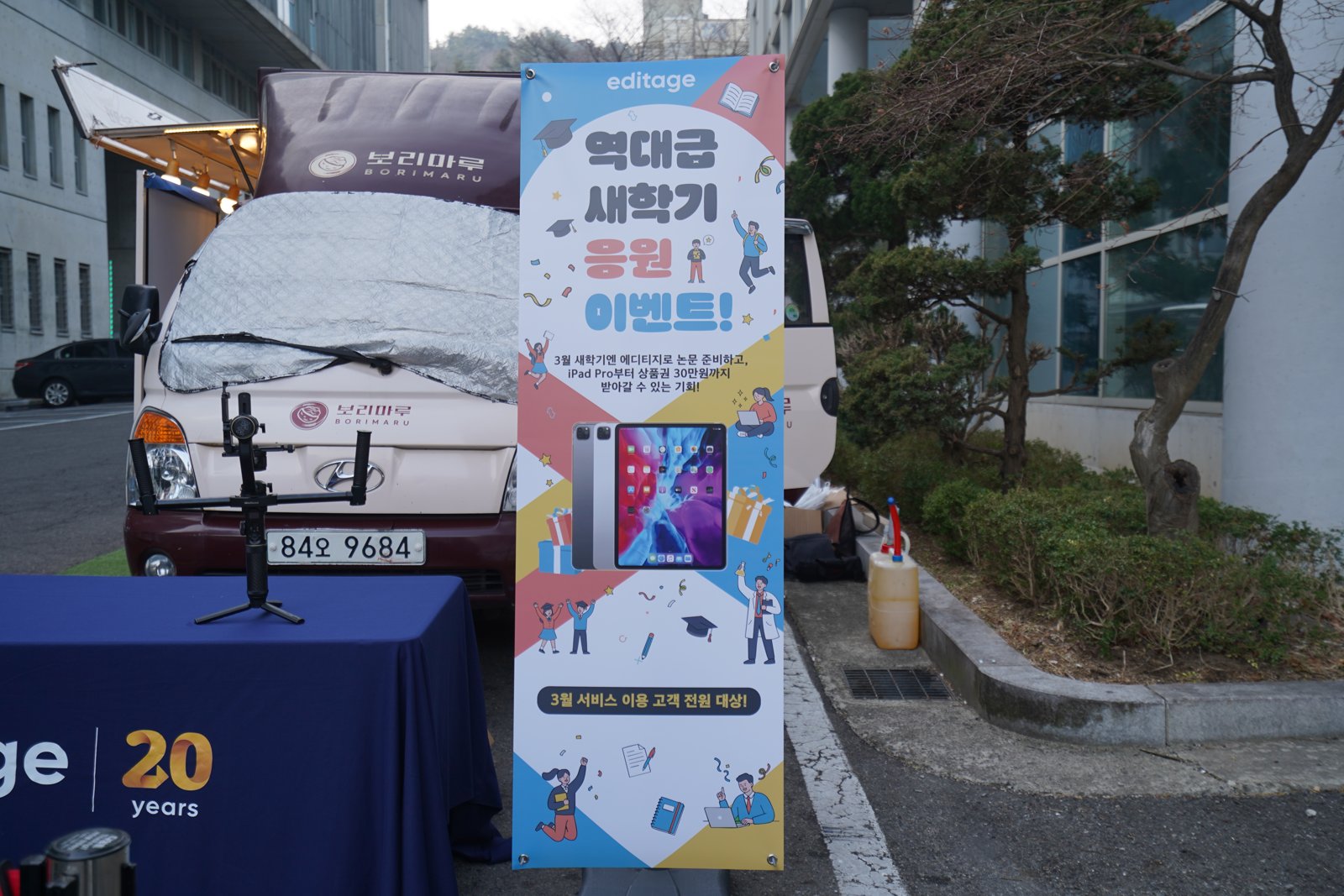 에디티지 로고와 역대급 새학기 응원 이벤트 문구, 아이패드 그림을 넣은 세로 X배너가 트럭 옆에 서 있다
